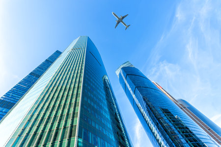 Modern glass skyscrapers on a clear day and passenger plane flies overの写真素材