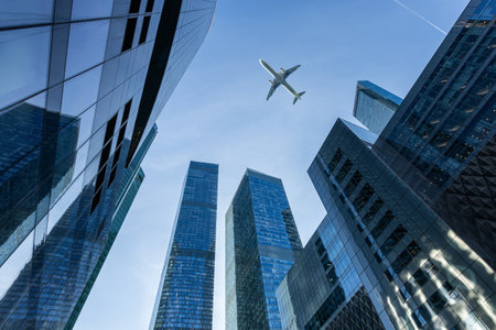 Modern glass skyscrapers on a clear day and passenger jet plane fly overの写真素材