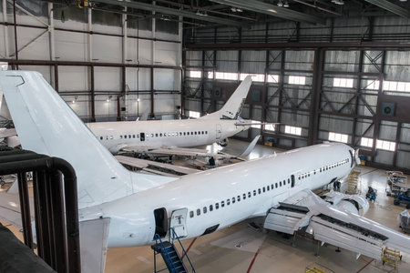 White passenger planes in the aviation hangar. Airplanes under maintenance. Checking mechanical...