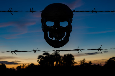 Silhouettes of Skull and Barbed wire on sunset background, Concept for Halloween background.の写真素材