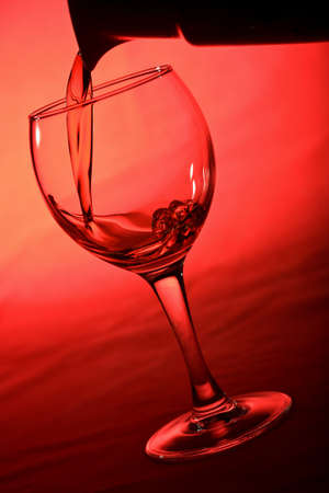 wine pouring into glass over red backgroundの写真素材