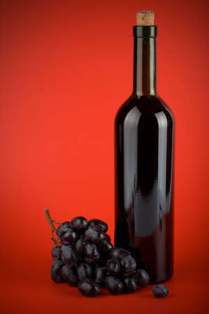 bottle of wine and grapes over red backgroundの写真素材