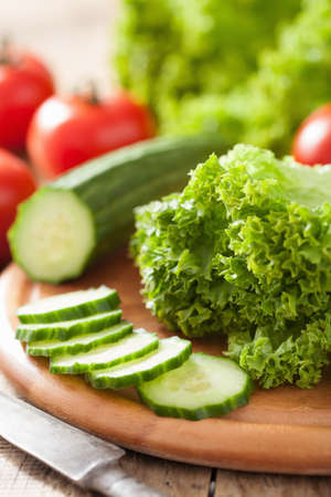 fresh cucumber tomatoes and salad leaves on chopping boardの写真素材