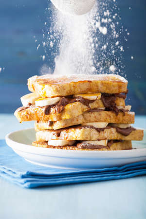 sprinkling powder sugar over french toasts with banana chocolate sauce caramel for breakfastの写真素材