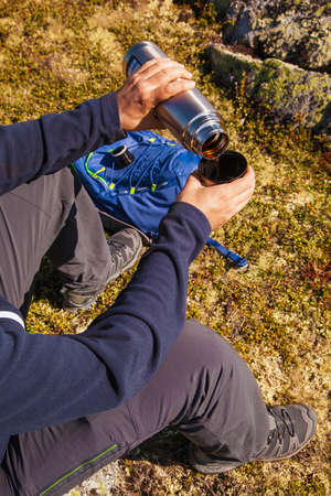 man holding thermos with hot tea outdoors. hiking and leisureの写真素材