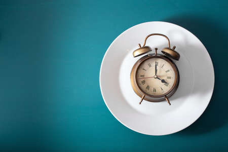 concept of intermittent fasting, ketogenic diet, weight loss. alarm clock on a plate