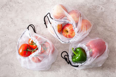 apples tomatoes bell peppers vegetables in reusable mesh nylon bag, plastic free zero waste conceptの写真素材