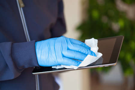 man hands in gloves disinfecting tablet computer screen, eliminate germs coronavirus bacteriaの写真素材