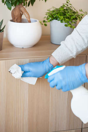 man hands in gloves disinfecting chest of drawers handle, killing virus on surfaceの写真素材