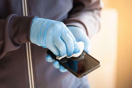 man hands in gloves disinfecting smartphone, eliminating germs coronavirus bacteriaの写真素材
