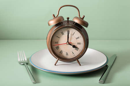concept of intermittent fasting, ketogenic diet, weight loss. fork and knife, alarmclock on plate