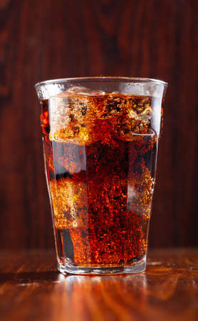 glass of cold cola soft drink with ice on wooden background