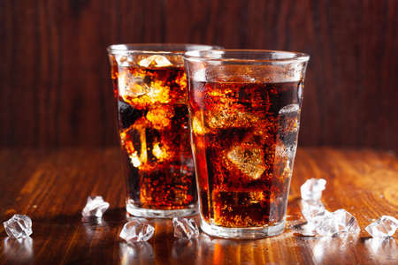 glass of cold cola soft drink with ice on wooden backgroundの写真素材