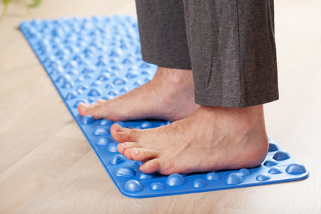 man doing flatfoot correction gymnastic exercise walking on massage mat at homeの写真素材