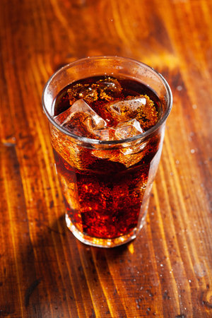 glass of cold cola soft drink with ice on wooden backgroundの写真素材