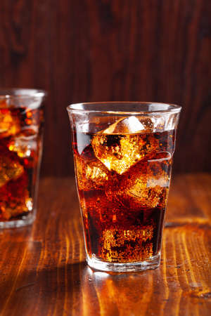 glass of cold cola soft drink with ice on wooden backgroundの写真素材