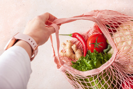 hand holding fruits vegetables in reusable mesh cotton bag, plastic free zero waste conceptの写真素材