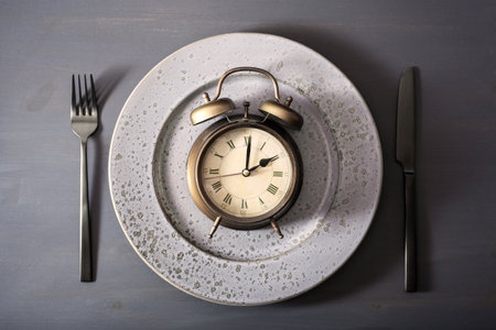 concept of intermittent fasting, ketogenic diet, weight loss. fork and knife on a plate and alarmclockの写真素材