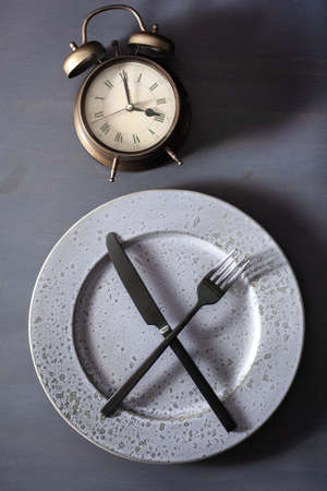 concept of intermittent fasting, ketogenic diet, weight loss. fork and knife on a plate and alarmclockの写真素材