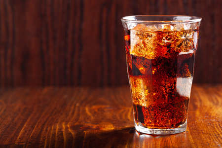 glass of cold cola soft drink with ice on wooden backgroundの写真素材