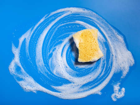 cleaning sponge wiping foam soap suds on blue background, household washing conceptの写真素材