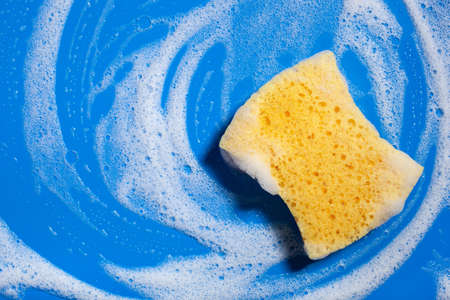cleaning sponge wiping foam soap suds on blue background, household washing conceptの写真素材