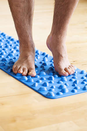 man doing flatfoot correction gymnastic exercise walking on massage mat at homeの写真素材