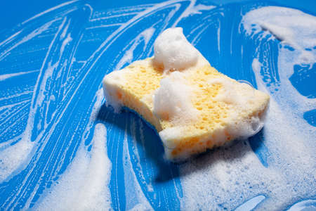 cleaning sponge wiping foam soap suds on blue background, household washing conceptの写真素材