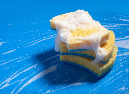 cleaning sponge wiping foam soap suds on blue background, household washing conceptの写真素材