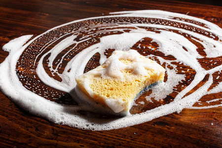 cleaning sponge wiping foam soap suds on wooden background, household washing concept