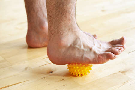 man doing flatfoot correction gymnastic exercise using massage ball at homeの写真素材