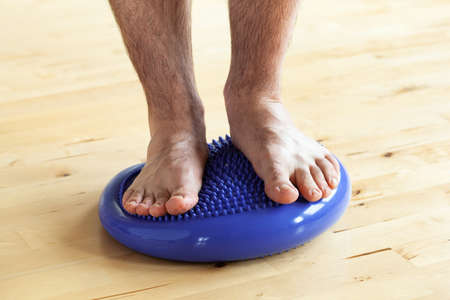 man doing flatfoot correction gymnastic exercise balancing on massage cushion at homeの写真素材