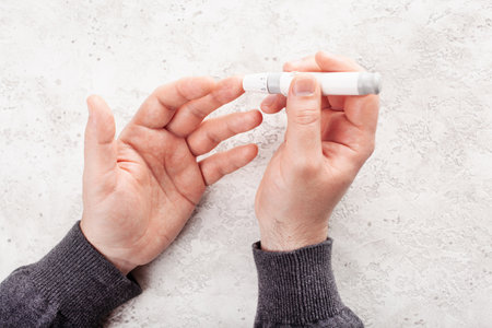 man hands using lancet on finger to check blood sugar or ketones level by glucose meter. medicine diabetes keto diet health care at homeの写真素材