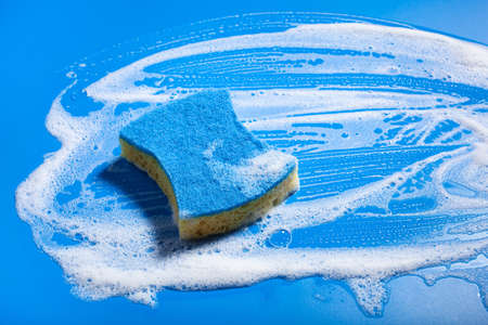 cleaning sponge wiping foam soap suds on blue background, household washing conceptの写真素材