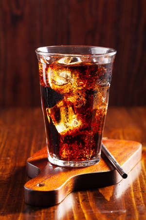 glass of cold cola soft drink with ice on wooden backgroundの写真素材