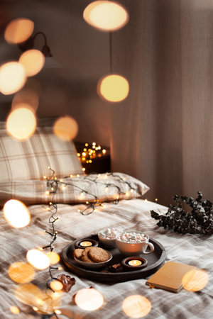 warm cozy bedroom winter or autumn interior with cup of hot chocolate on tray, candles christmas lightsの写真素材