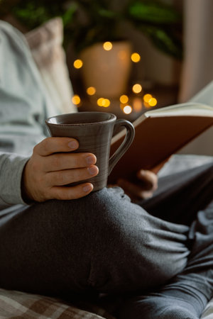 A caucasian man relaxing at home, reading a book, drinking coffee in bedの写真素材