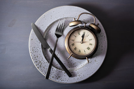 concept of intermittent fasting, ketogenic diet, weight loss. fork and knife, alarmclock on plate