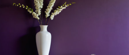 Elegant plant with white and purple flowers in a white vase, placed against a rich purple wall. Perfect for interior design and floral decor themes.の素材
