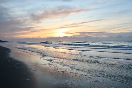 A scenic sunset over the beach of Vlieland, Netherlands, with gentle waves and colorful reflections on the wet sand creating a calm coastal atmosphere.の写真素材
