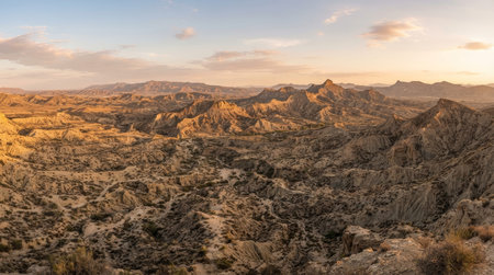 Wide realistic panoramic landscape of the Tabernas Desert in Almeria, expansive full scene featuring dry ravines, rugged hills and expansive semi arid landscapes in calm golden hour weather, no people, no text, no logo, no watermark.