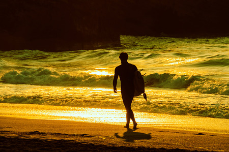 Surfer walking on the beach in the evening light, cross processed effectの写真素材
