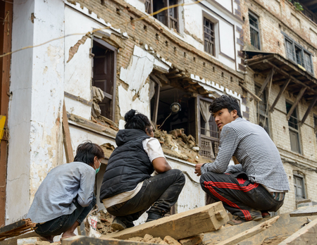 KATHMANDU, NEPAL - APRIL 26, 2015: Three young men squatting down on a pile of rubble at Durbar Square which was severly damaged after the major earthquake on 25 April 2015.のeditorial素材
