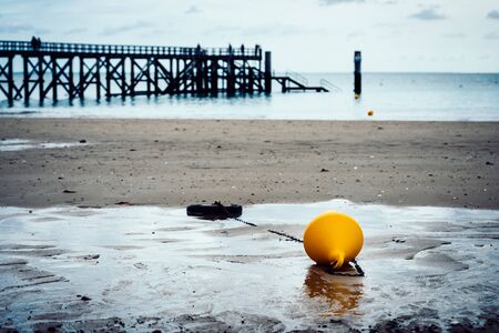 Orange buoy on a beach, pier in the background in Noirmoutier, France. Film emulation filter applied.の写真素材