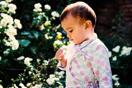 Baby boy wearing traditional Nepali daura bhoto plays with white flowers in gardenの写真素材