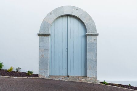 Light blue arched door with stone frame and white wall.の写真素材
