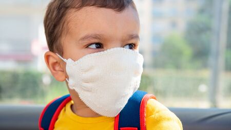 Little boy wearing white knitted cotton face mask as a protection against the novel coronavirus and Covid-19 disease.の写真素材