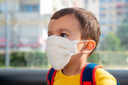 Little boy wearing white knitted cotton face mask as a protection against the novel coronavirus and Covid-19 disease.の写真素材