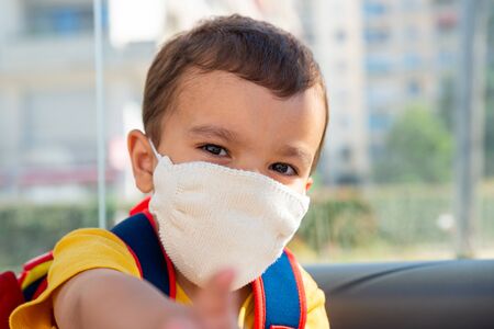 Little boy wearing white knitted cotton face mask as a protection against the novel coronavirus and Covid-19 disease.の写真素材