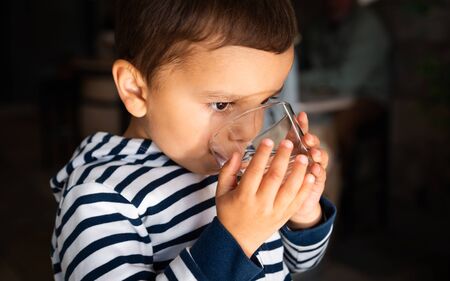 Cute little boy drinking water from a glassの写真素材
